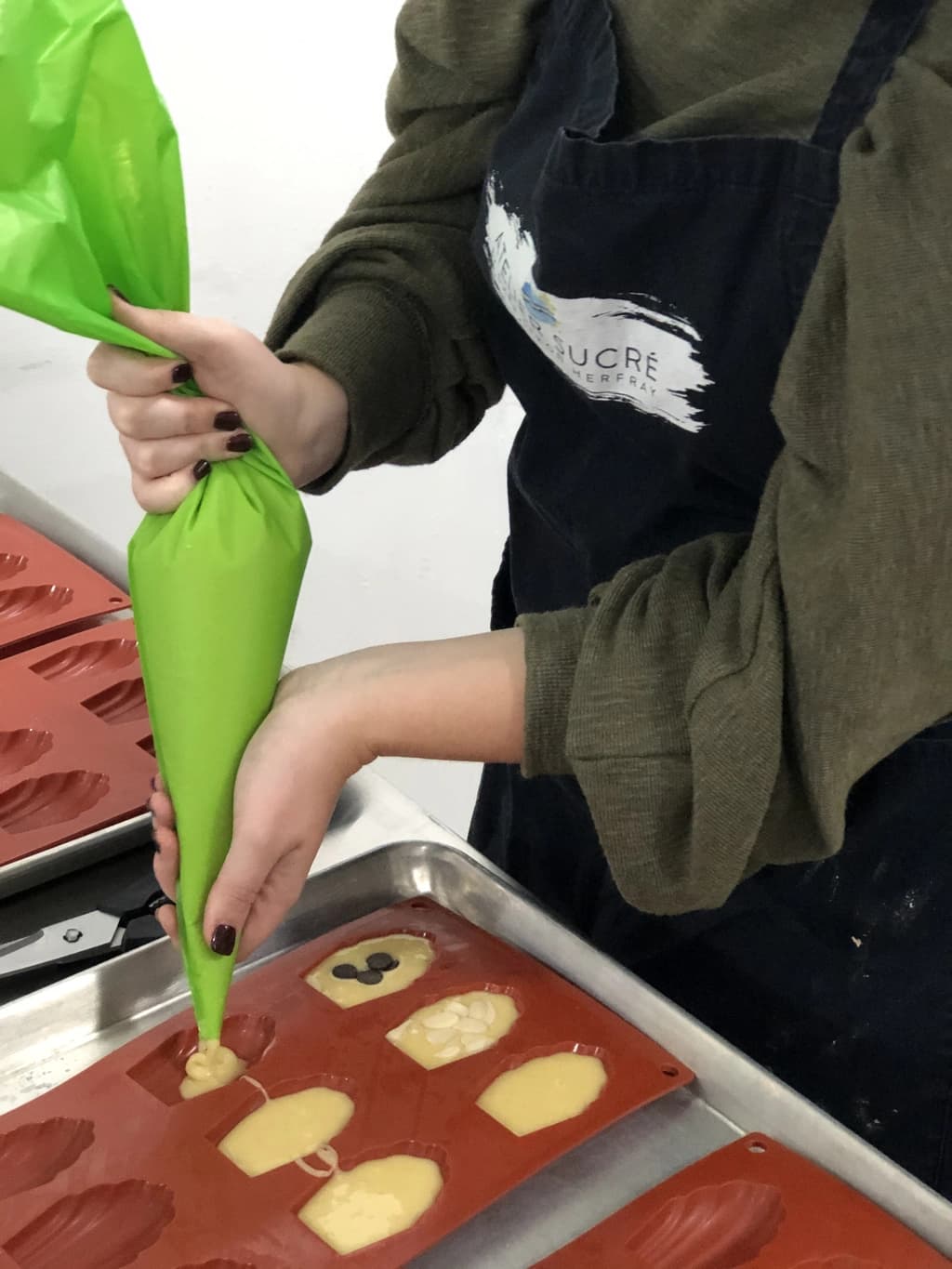 Person piping chocolate into molds from a green piping bag, wearing a branded apron.