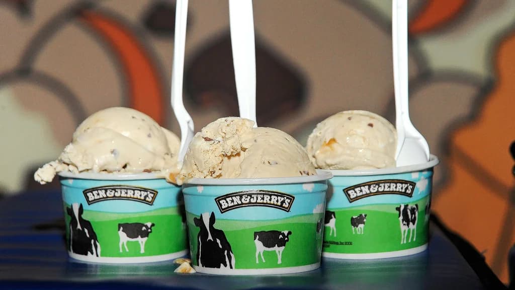 Three cups of Ben & Jerry's ice cream with spoons, each filled with scoops of creamy ice cream, set against a colorful background.