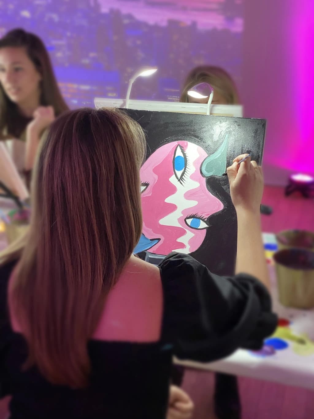 Participants seated at tables, painting abstract art, while surrounded by projections of Picasso's work displayed on large walls.