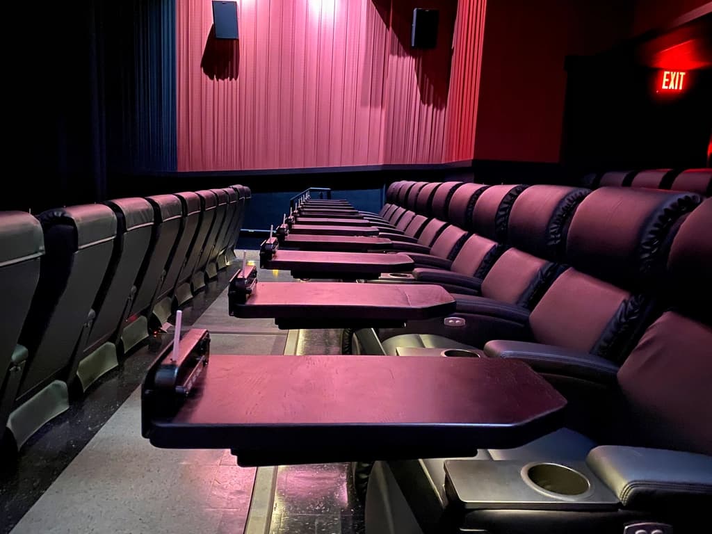Comfortable movie theater seats with attached trays in a dimly lit theater, ready for an immersive viewing experience.