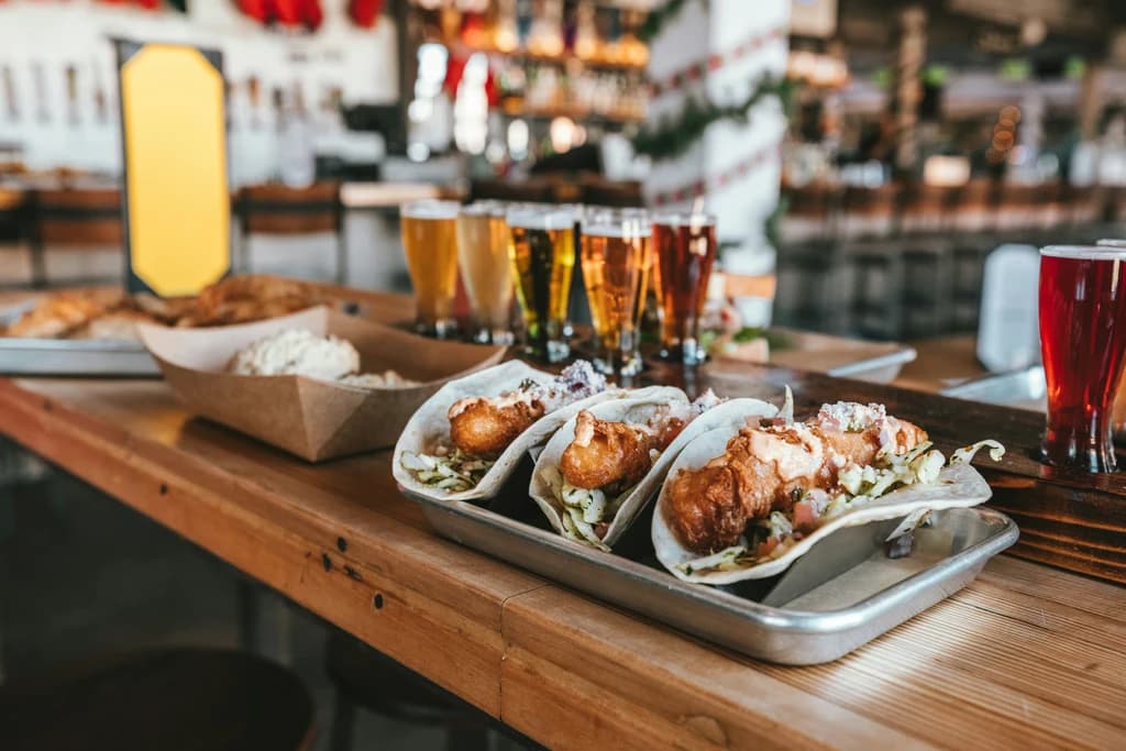 a tray of tacos at a bar top with a flight of beers