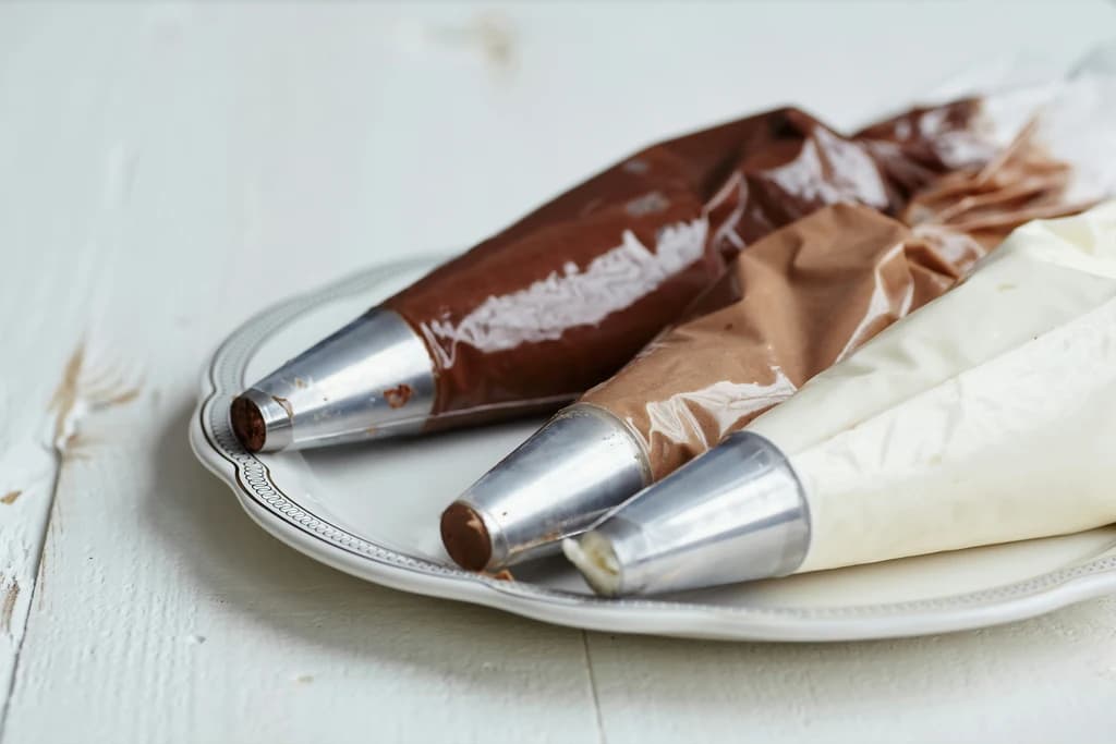 Piping bags filled with chocolate and vanilla cream ready for truffle decorating on a white plate.