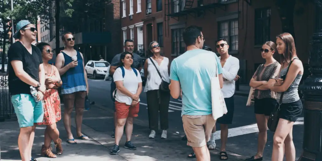 a man standing and talking in front of a group of people on a street