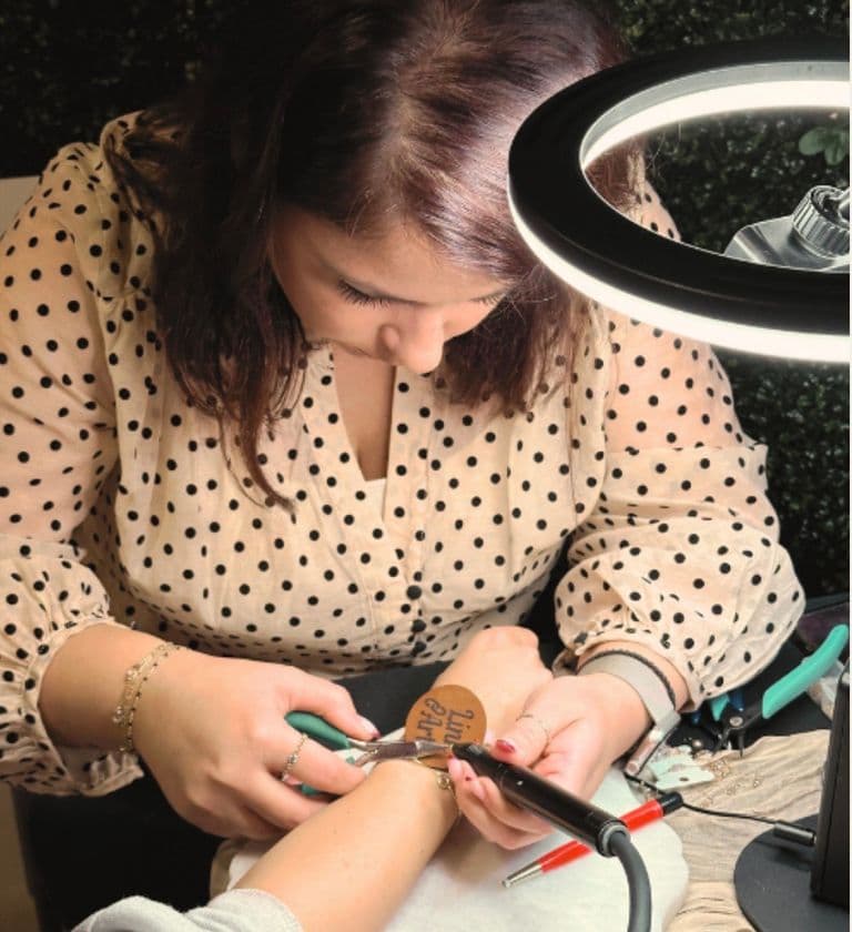 Jewelry artist welding permanent bracelet onto client’s wrist under ring light