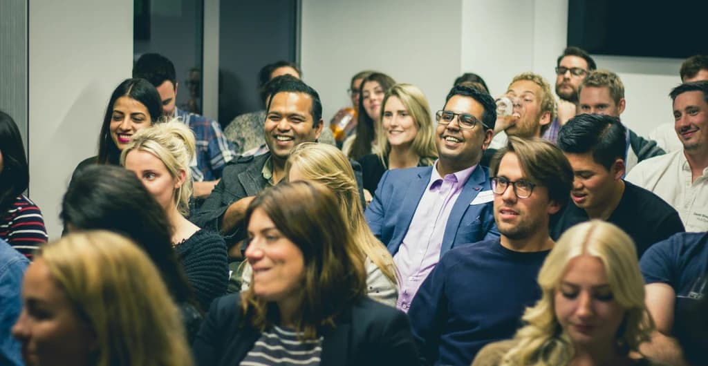 a crowd smiling and laughing at a speaker on stage