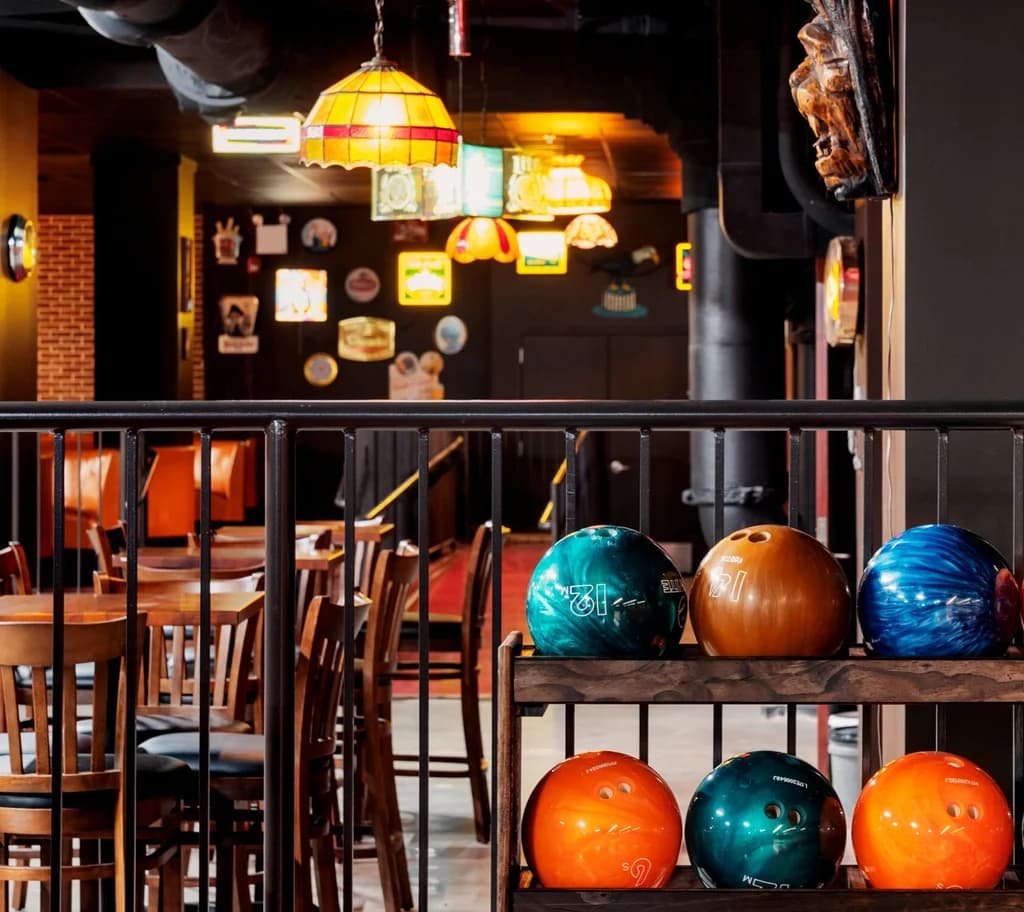 Bowling balls on a rack in a retro-themed bowling alley, with colorful lamps and wooden seating creating a nostalgic ambiance.