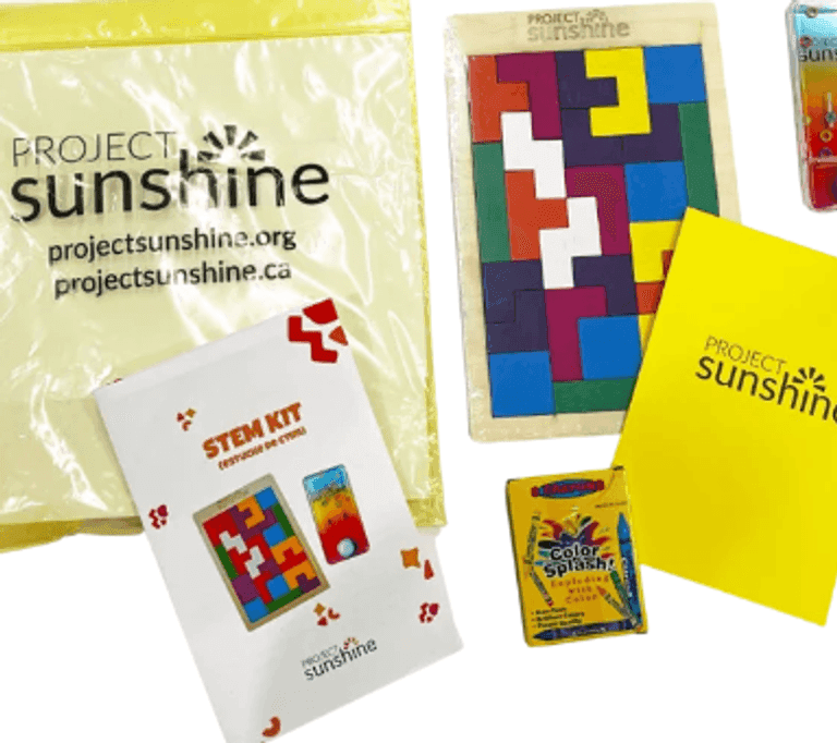 A Project Sunshine activity kit including a yellow zip bag, a STEM kit booklet, a wooden puzzle with colorful geometric pieces, crayons, a card game, and a yellow folder.