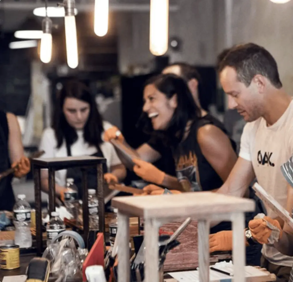 a group of people laughing and working on a metal project at a table