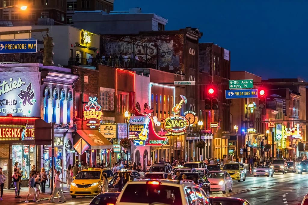 Night view of Broadway in Nashville, filled with neon signs, live music venues, and crowds walking along the street, capturing the vibrant nightlife.