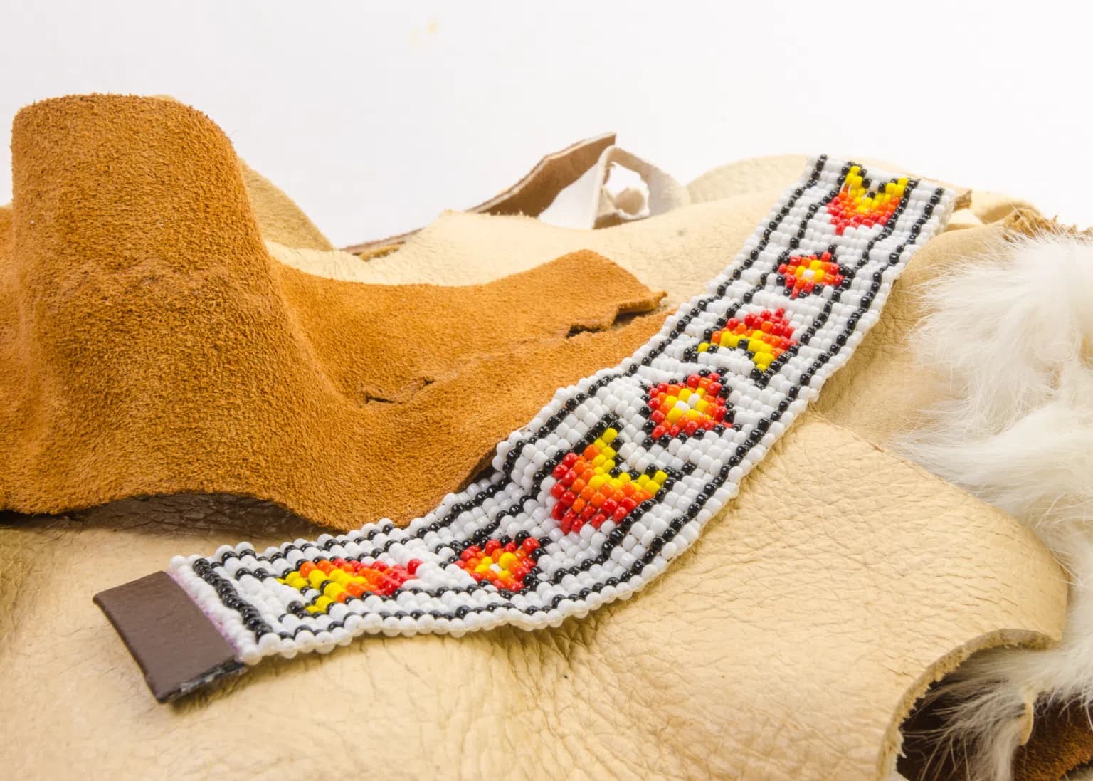 A beautifully crafted Native American beaded bracelet featuring intricate red, yellow, and black patterns on a bed of leather material.