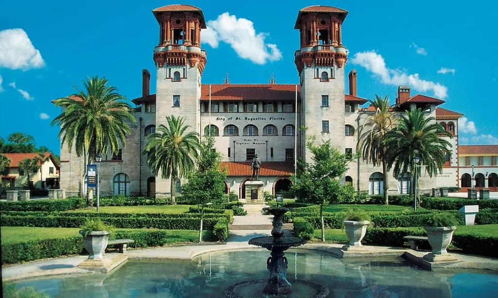 Historic building with twin towers, lush gardens, and a central fountain in St. Augustine, Florida, under a clear blue sky.