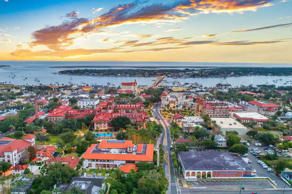 Aerial view of St. Augustine, Florida, showcasing a colorful sunset, coastal landscape, and historic architecture with a scenic harbor.