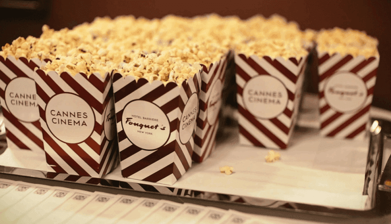 Striped Cannes Cinema popcorn boxes filled with popcorn on a silver tray.