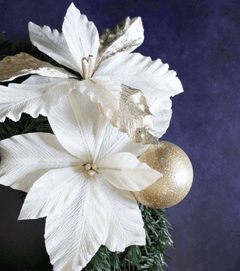 White and gold paper poinsettias with glitter ornament on a holiday wreath.