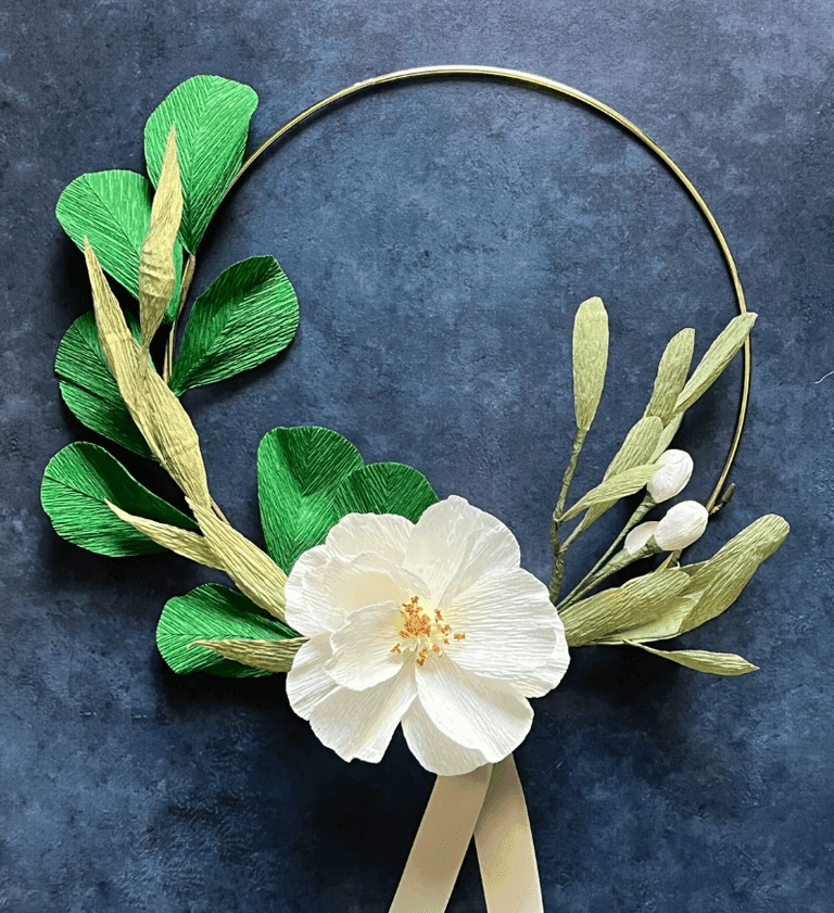 Minimalist wreath with green leaves, white paper flower, and gold hoop.