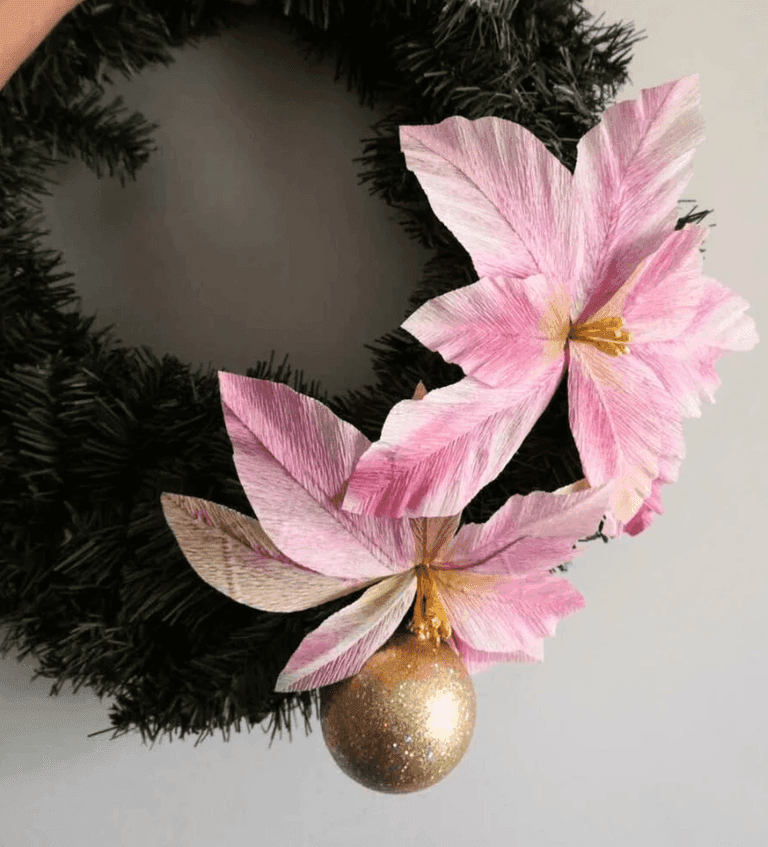 Pink paper poinsettias with gold glitter ornament on a wreath.