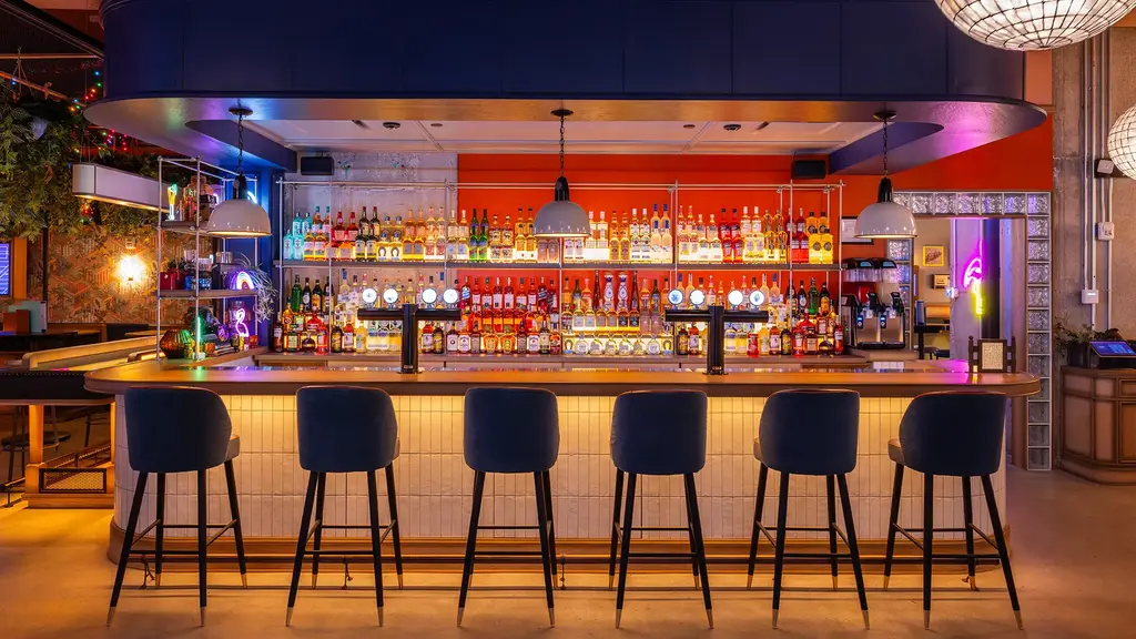 Stylish bar area with a wide selection of drinks and modern seating, illuminated by warm and inviting lighting.