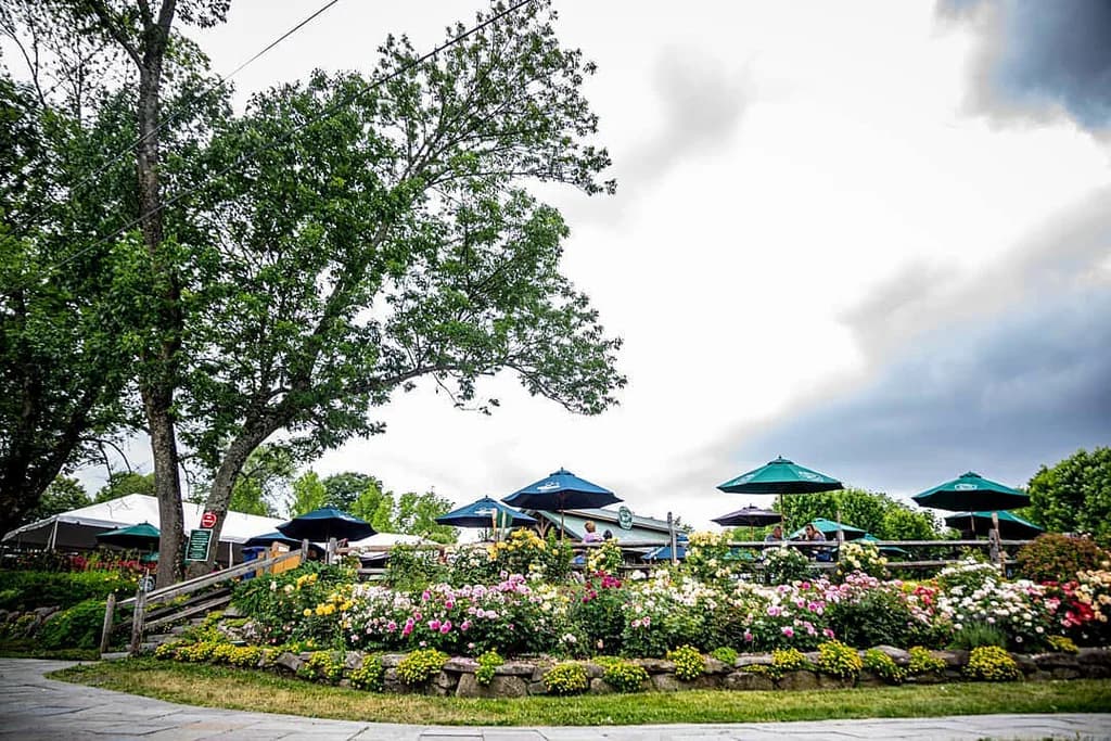 patio with tables and umbrellas surrounded by flowers and trees