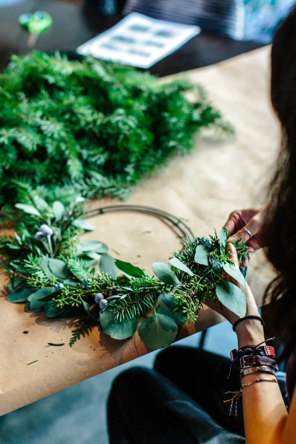 Close-up of a person’s hands carefully arranging eucalyptus leaves and other greenery onto a wreath frame during a wreath-making workshop.