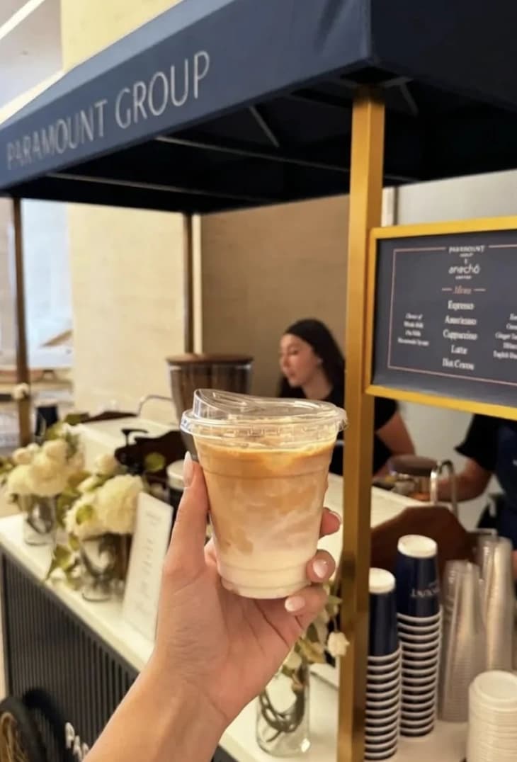 Hand holding iced coffee at Paramount Group coffee cart with barista